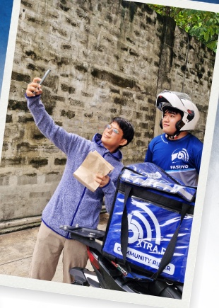 A customer takes a selfie with a bXTRA Community Rider and his branded delivery box — real photo